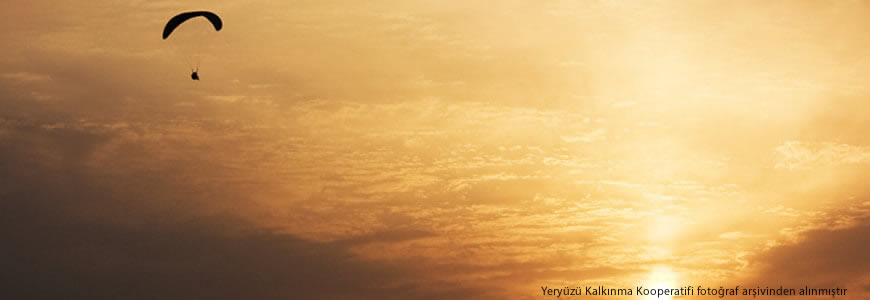 Gün batımının turuncuya çalan renklerinde güneşe doğru ilerleyen bir yamaç paraşütünün huzur duygusu uyandıran fotoğrafı